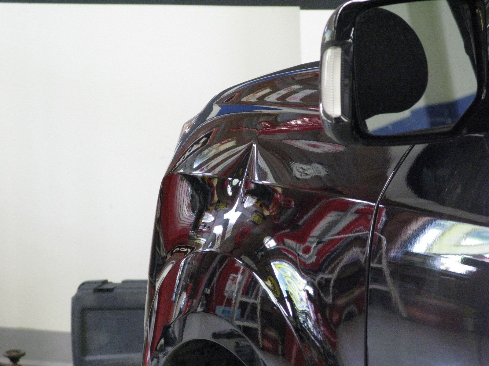 A black car with a damaged fender is parked in a garage