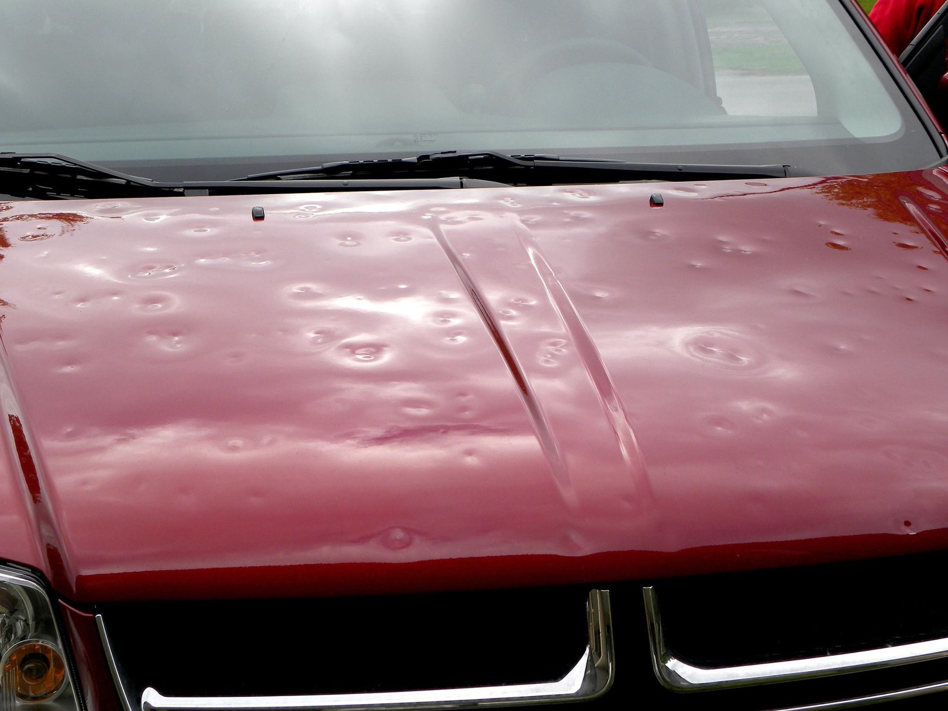 A red car with hail damage on the hood