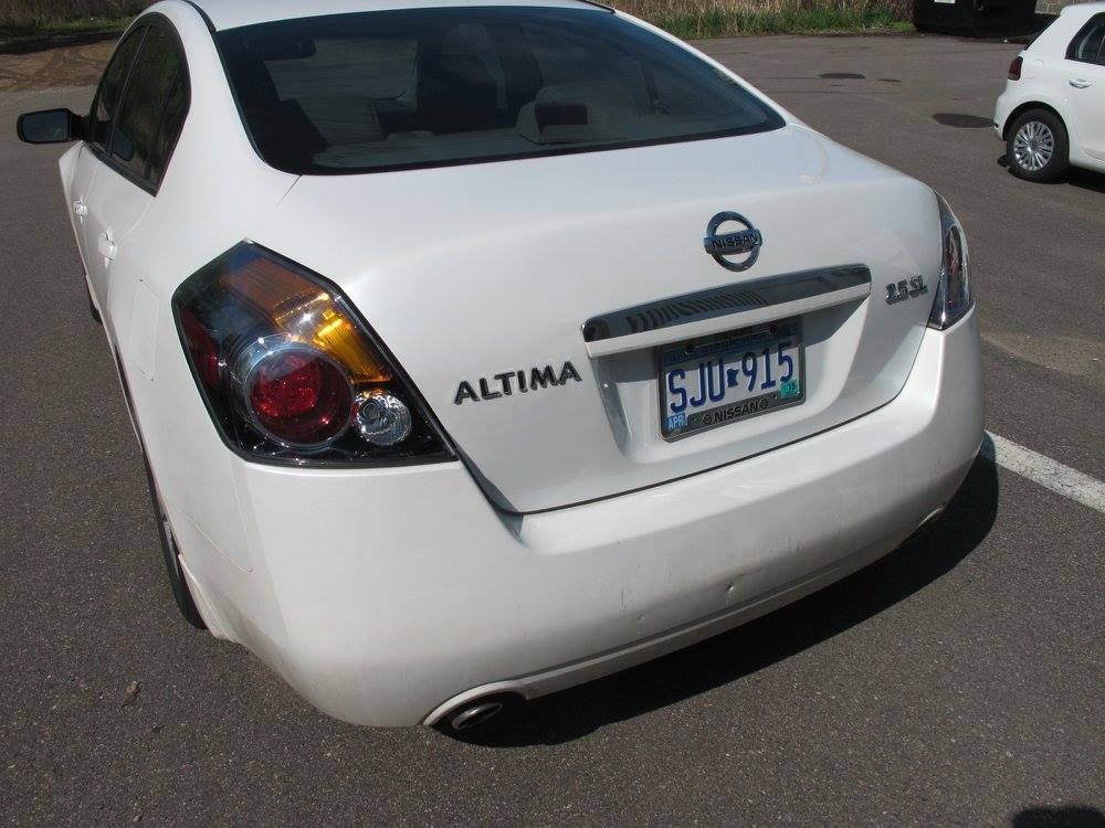 A white nissan altima is parked in a parking lot