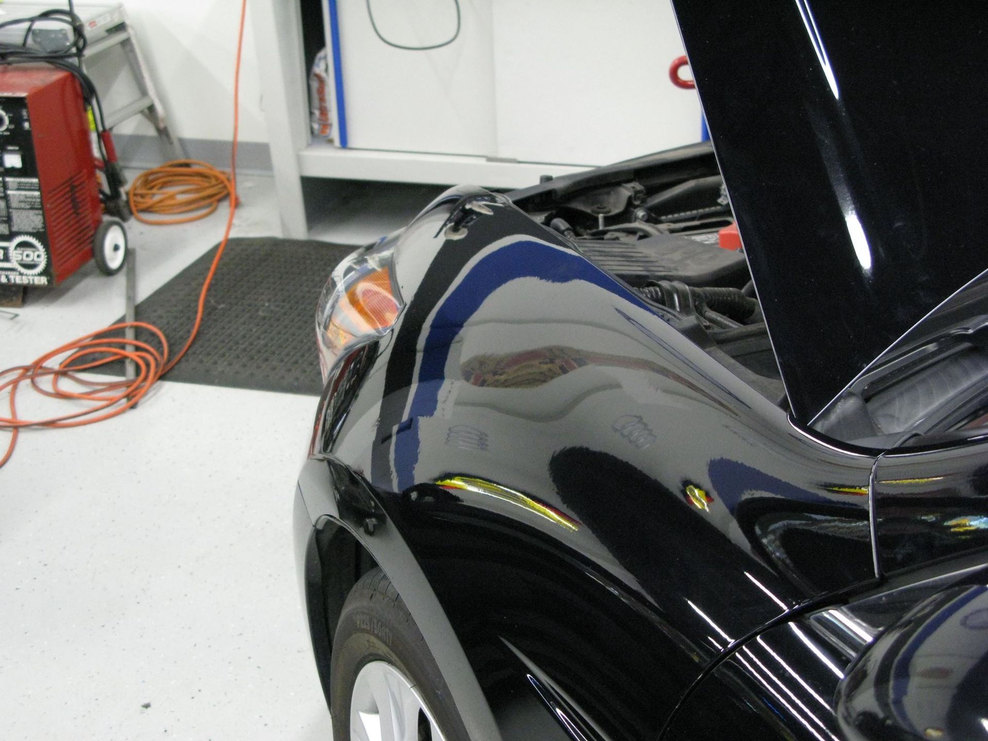 A black car with the hood up in a garage