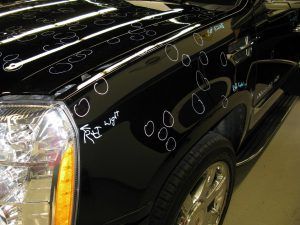 A black car with a lot of dents on it is parked in a garage.