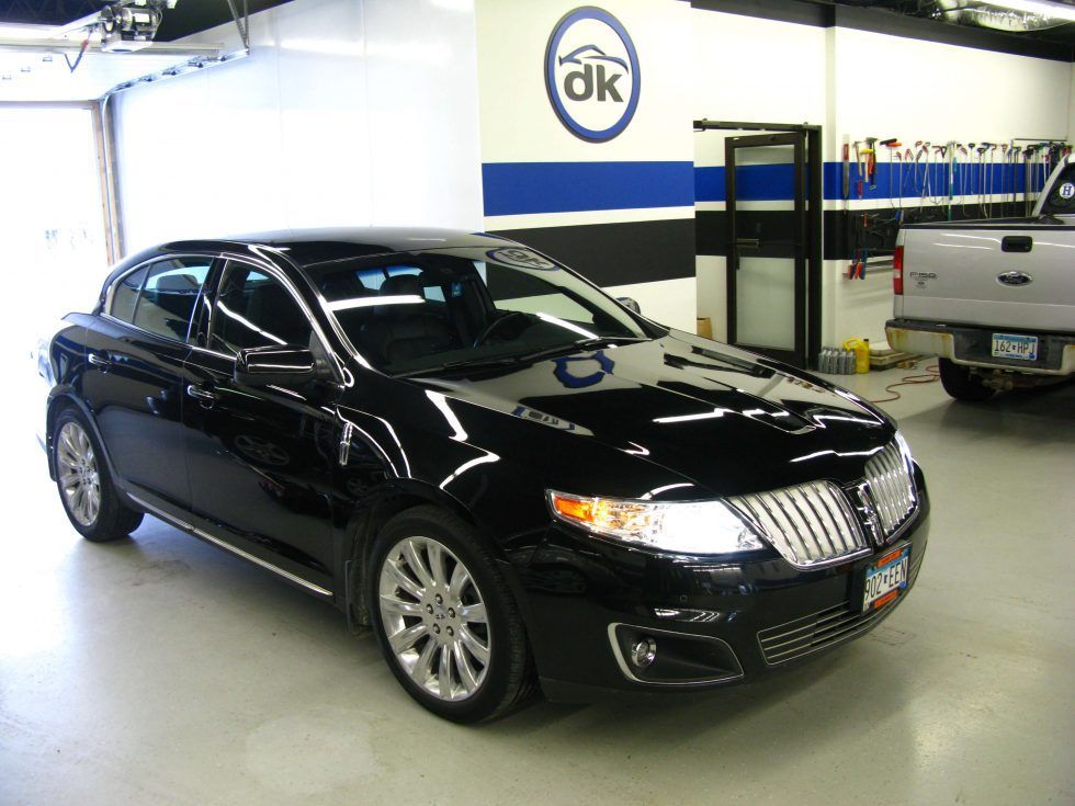 A black car is parked in a garage with a dk logo on the wall