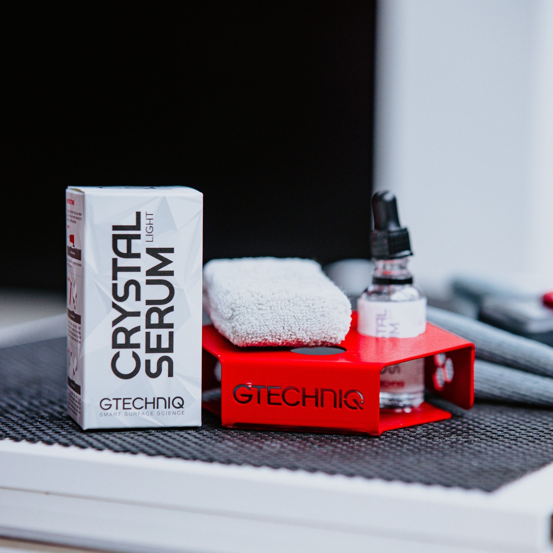 Gtechniq Crystal Serum Light kit: serum bottle, applicator, and box, on a red stand.