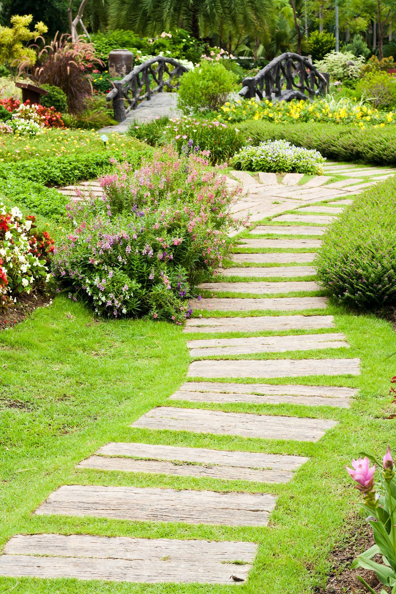 A stone walkway leading to a bridge in a garden