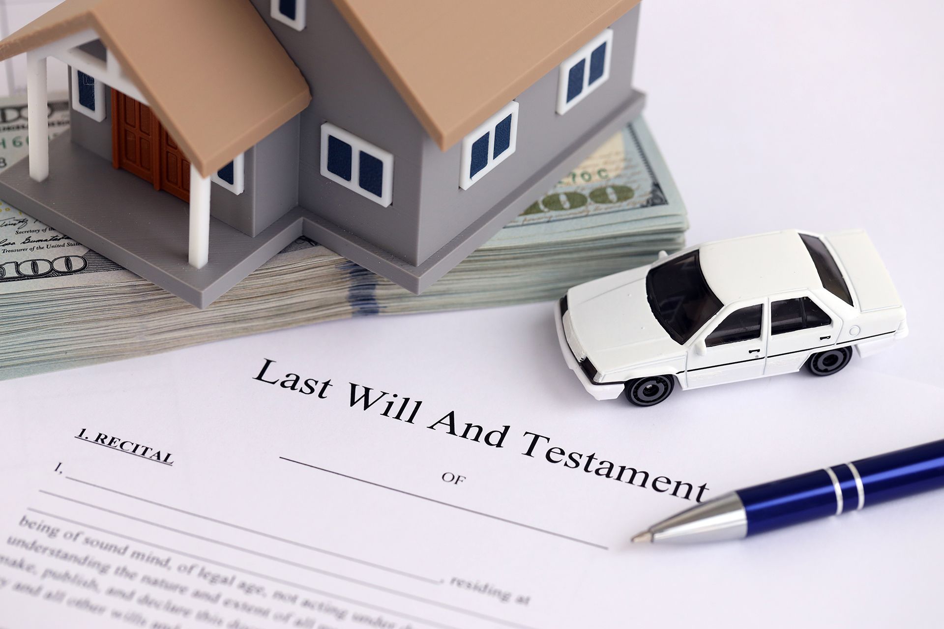 Miniature house and car on a Last Will and Testament document, with a pen and cash.