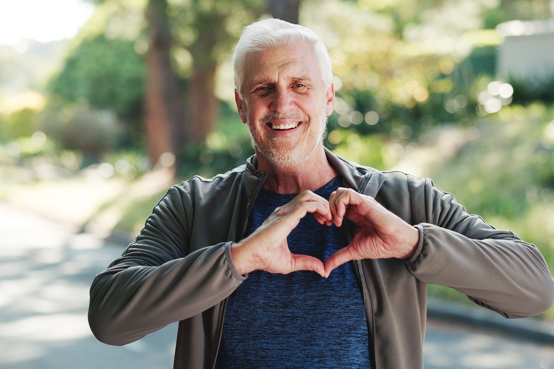 Man outdoors making a heart shape with his hands, smiling.
