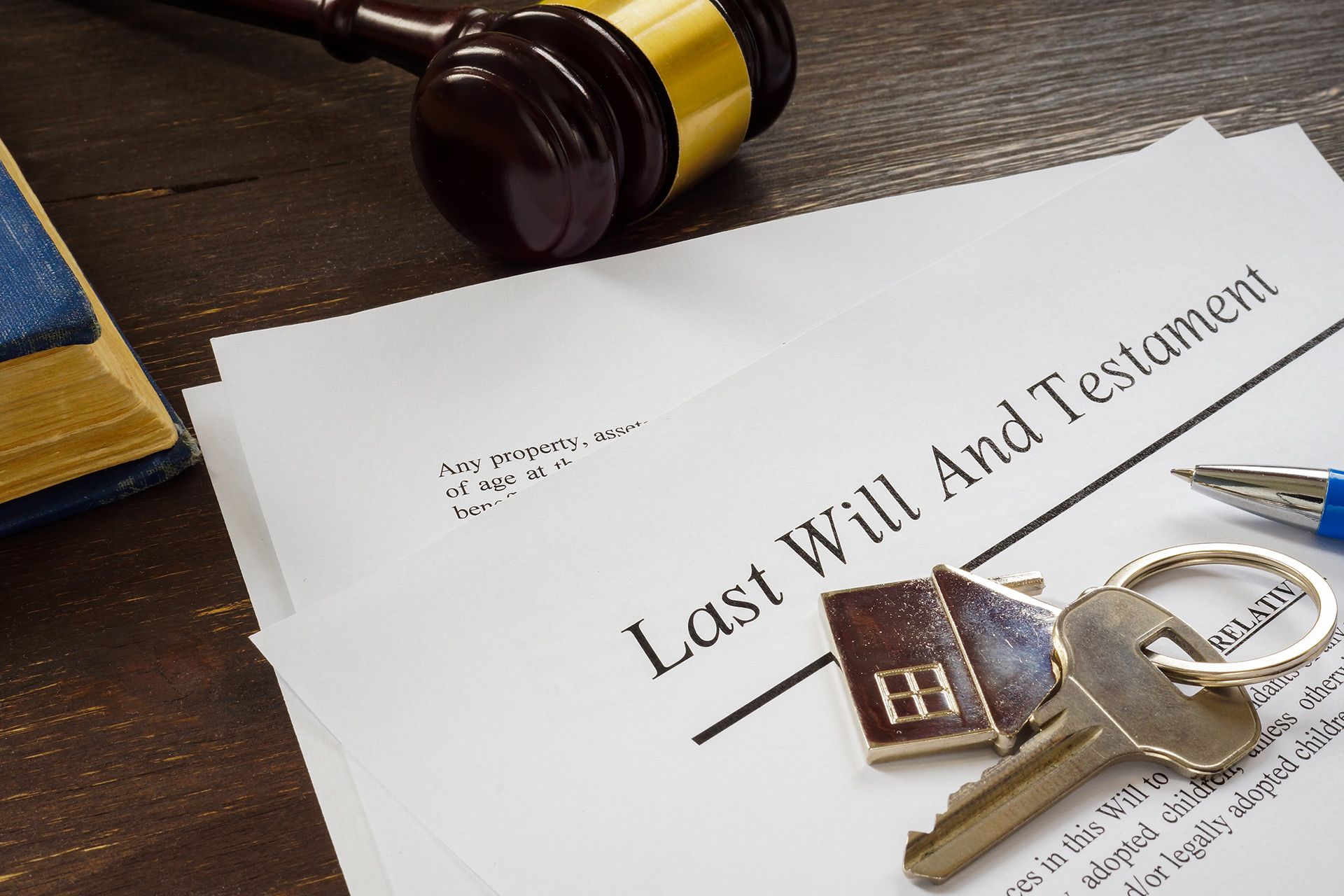 Last Will and Testament document with keys, gavel, and pen on a wooden surface.