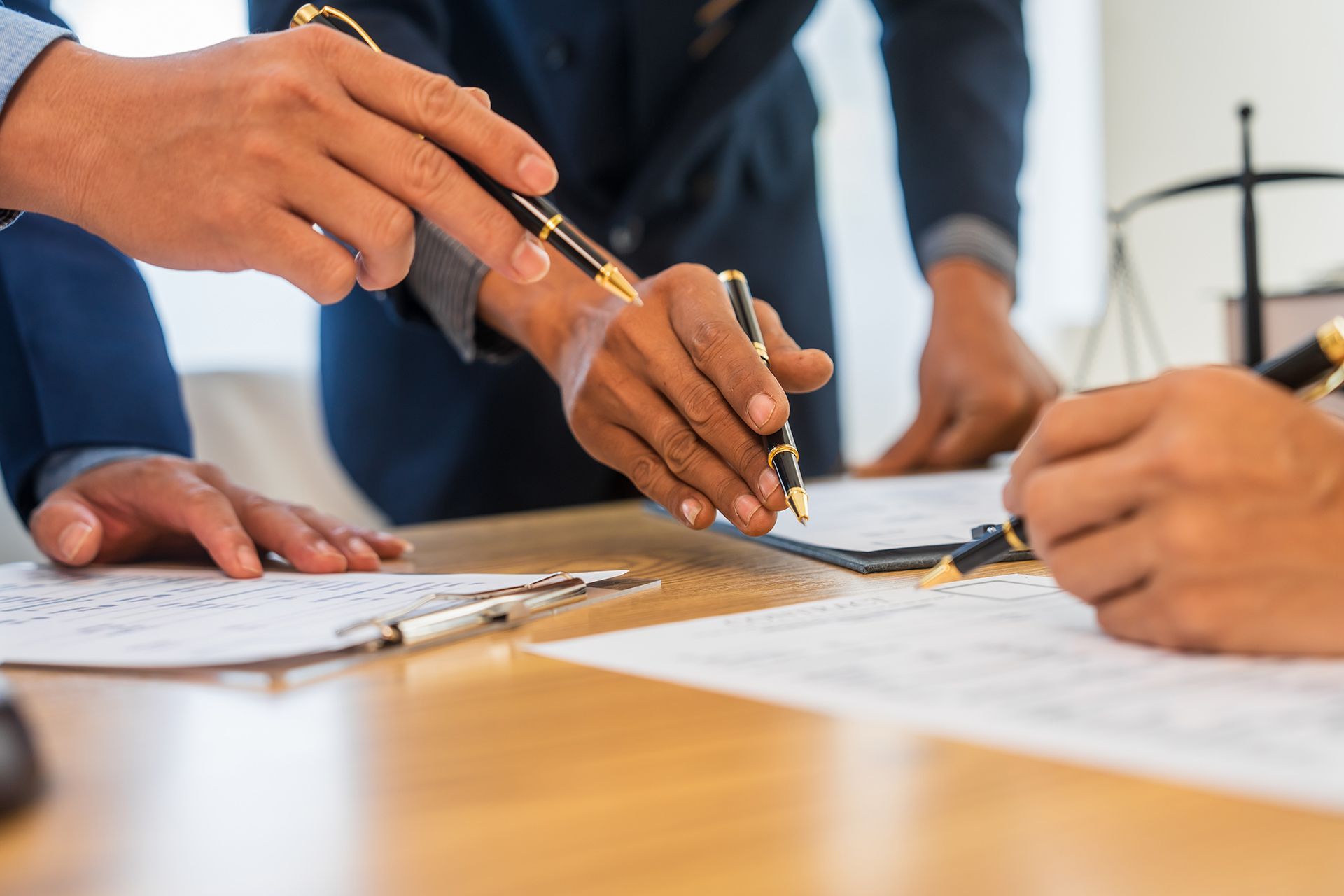 People in suits pointing at documents on a wooden table, discussing a legal matter.