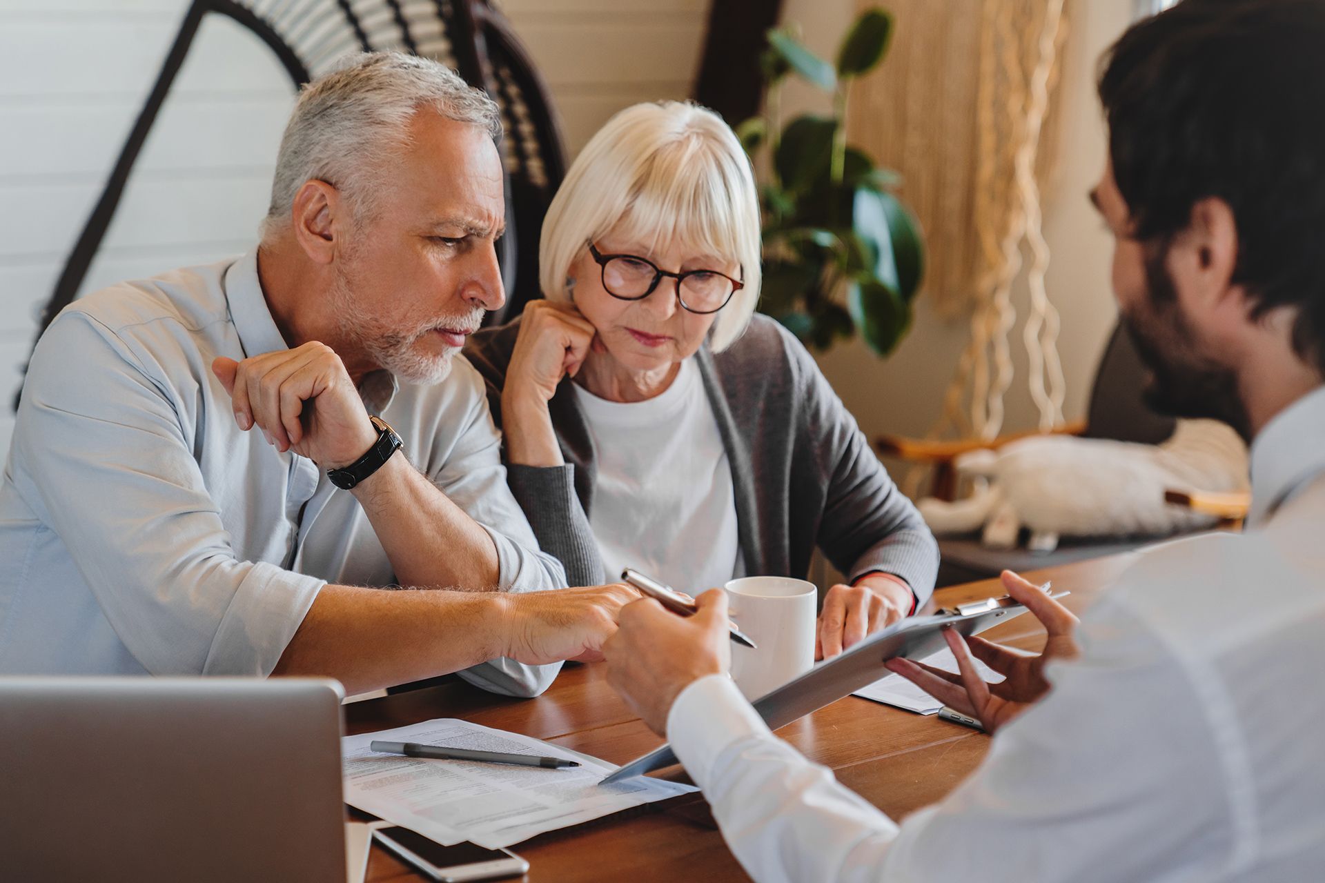 Older couple reviews documents with advisor, interior setting.