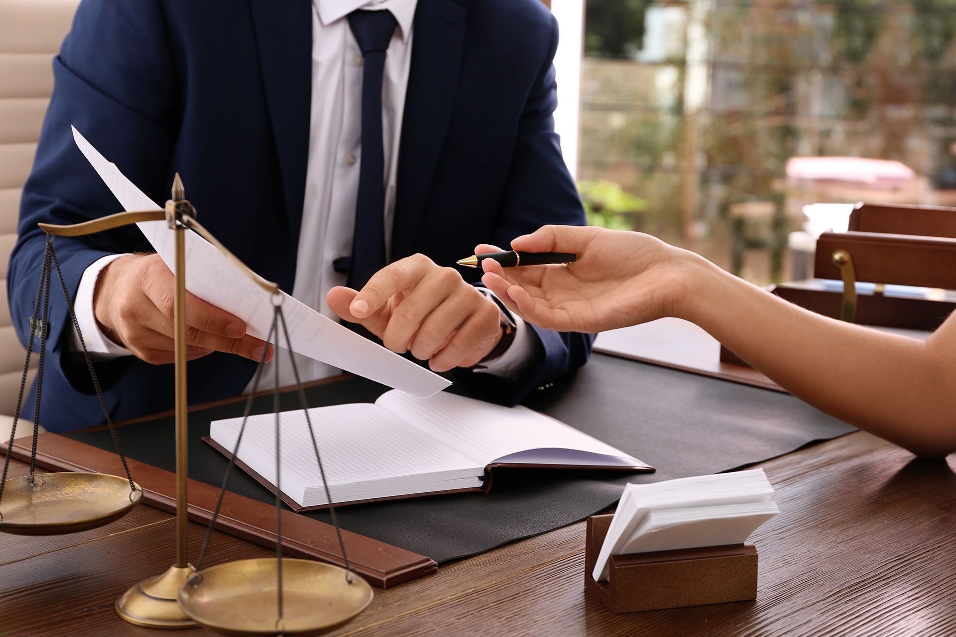 Lawyer in a suit presenting documents to a person; scales of justice on the table.