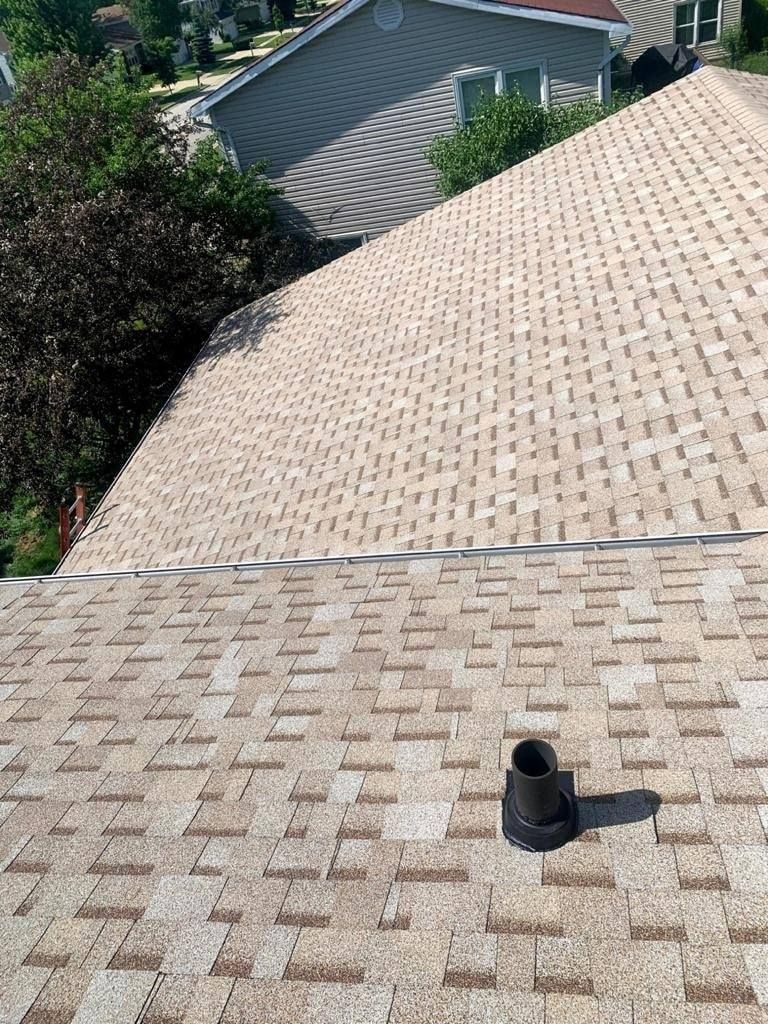 A roof with a chimney on it and a house in the background.