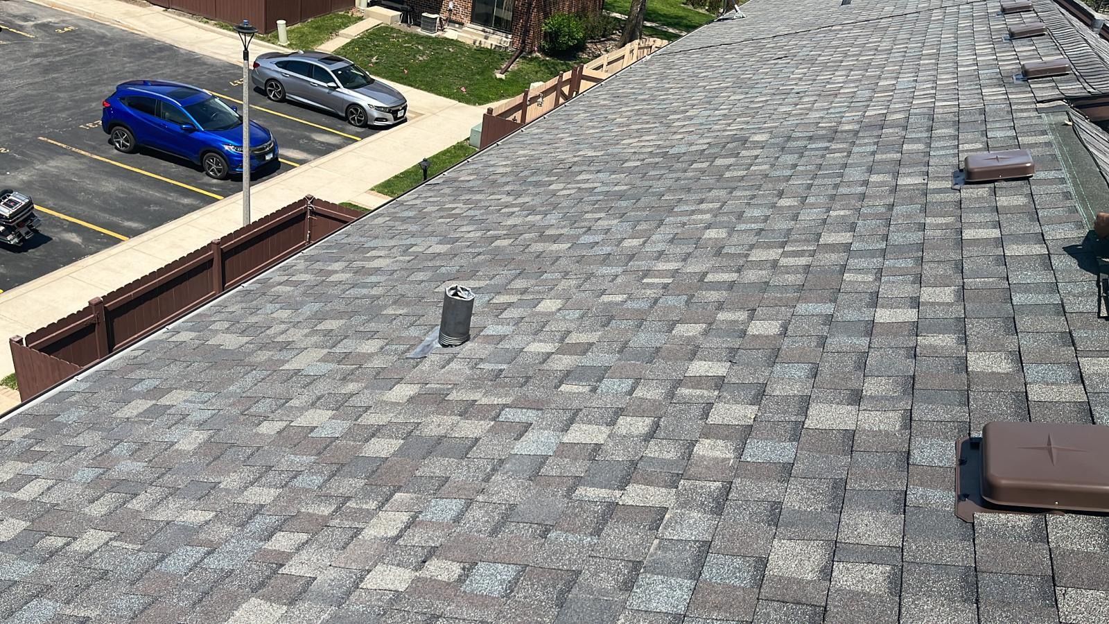 A roof with a lot of shingles on it and a parking lot in the background.