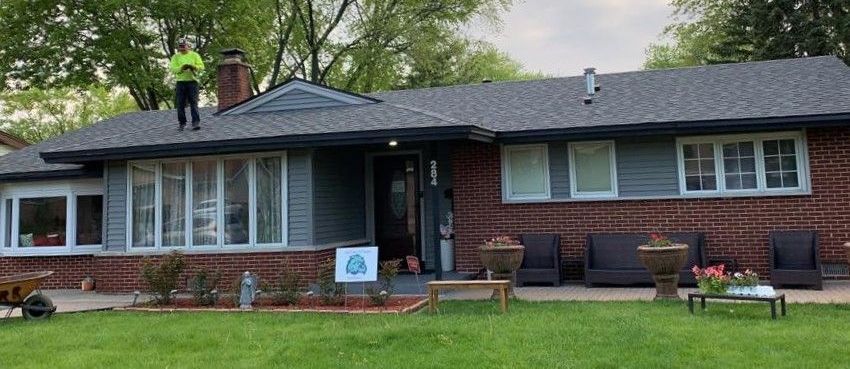 A man is standing on the roof of a brick house.
