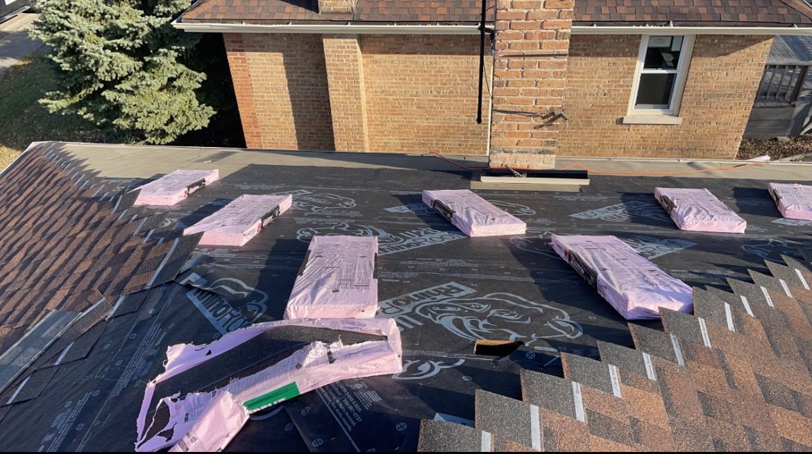 A roof with a lot of pieces of foam on it and a brick house in the background.