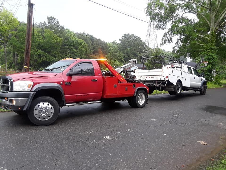 A red tow truck is pulling a white truck down a road.
