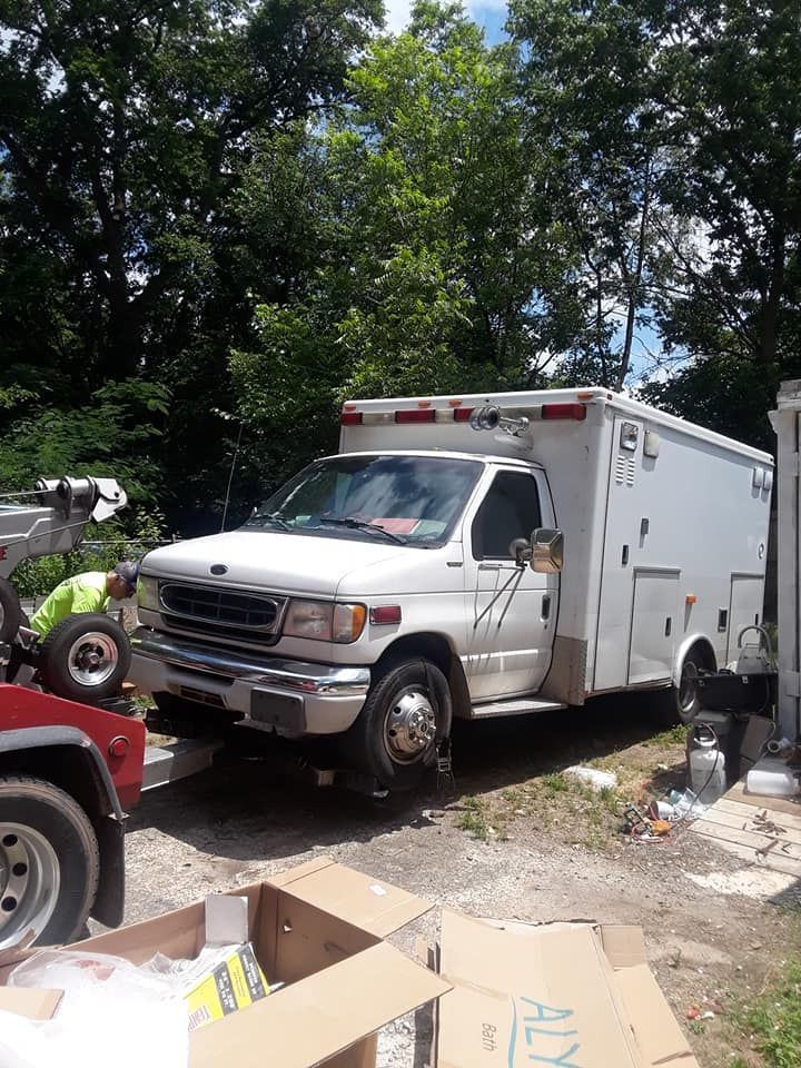 A white ambulance is parked in a driveway next to a tow truck.