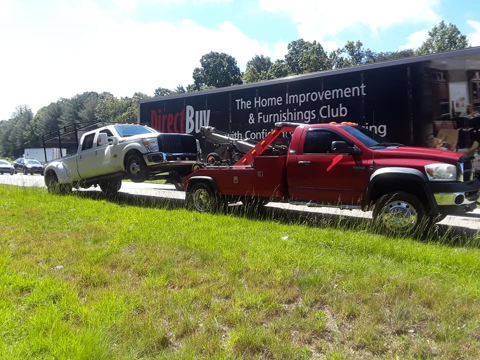 A red tow truck is towing a white truck on the side of the road.