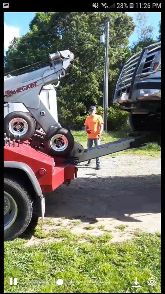 A man is standing next to a tow truck that is towing a truck.