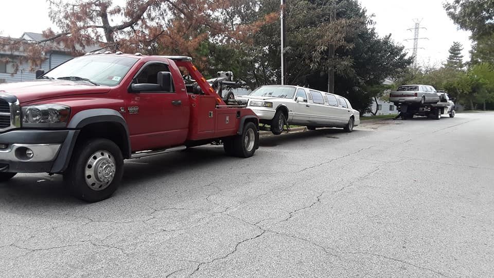A red tow truck is towing a white limousine down a street.