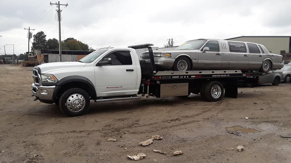 A tow truck is carrying a limousine on the back of it.