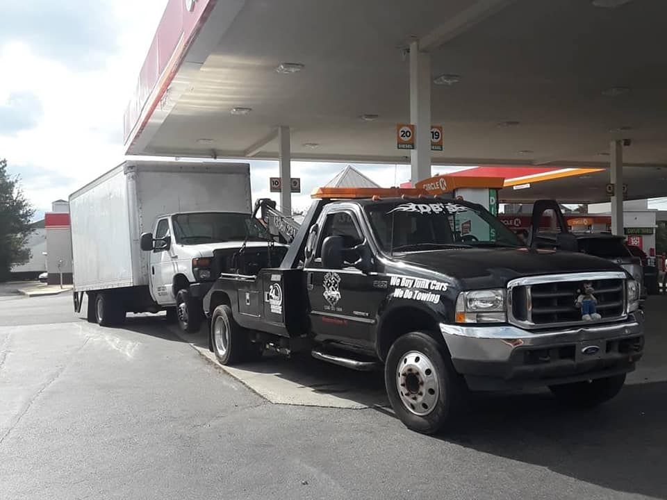 A tow truck is towing a white truck in a gas station.