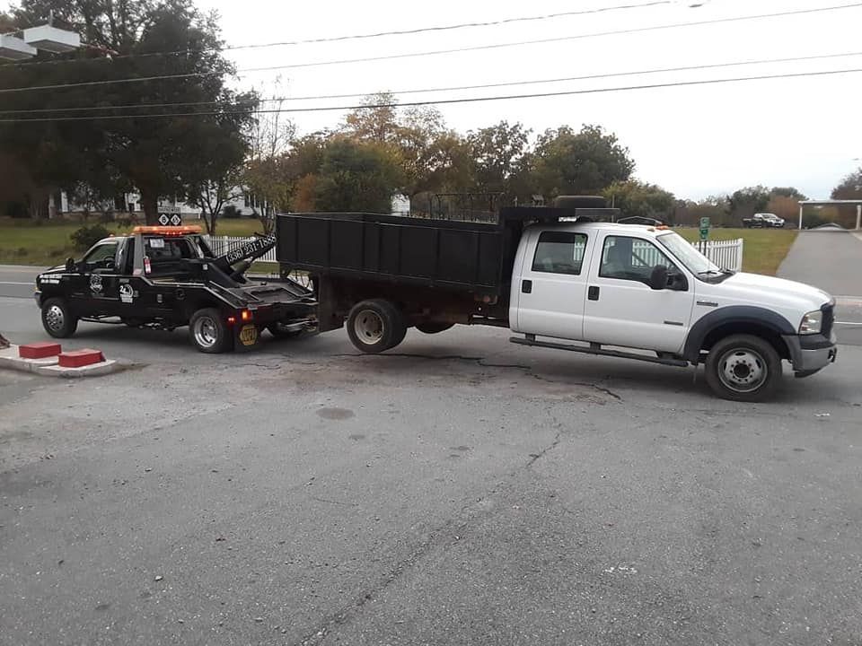 A white truck is being towed by a black tow truck