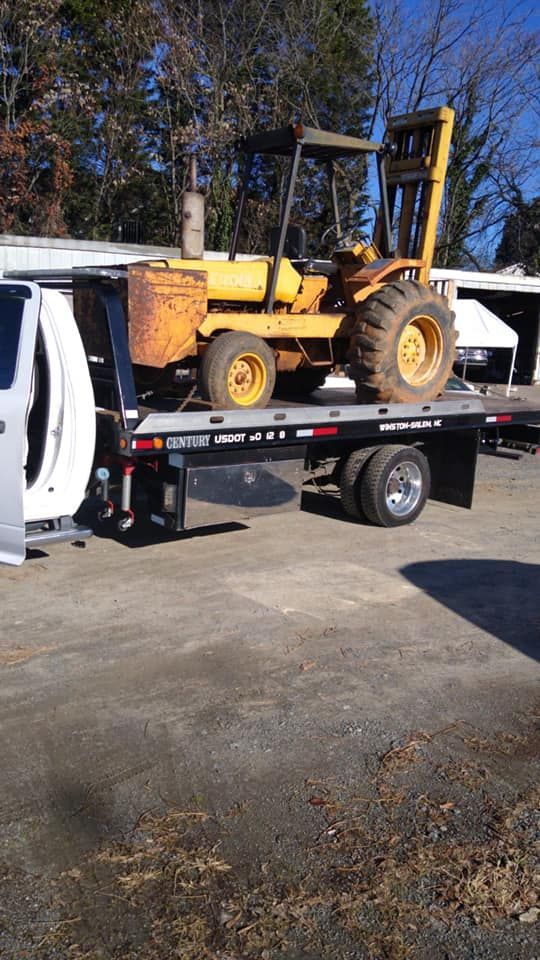 A yellow forklift is sitting on top of a flatbed tow truck.