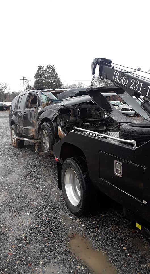 A tow truck is towing a damaged car in a parking lot.