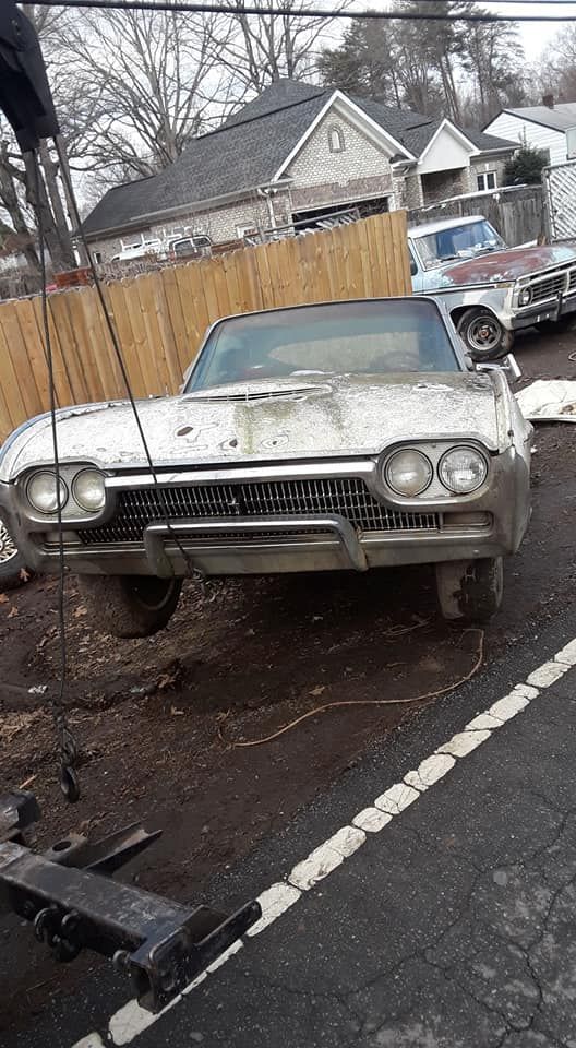 A white car is parked on the side of the road next to a wooden fence.