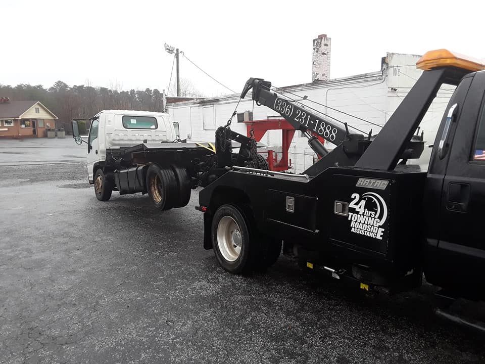 A black tow truck is towing a white truck in a parking lot