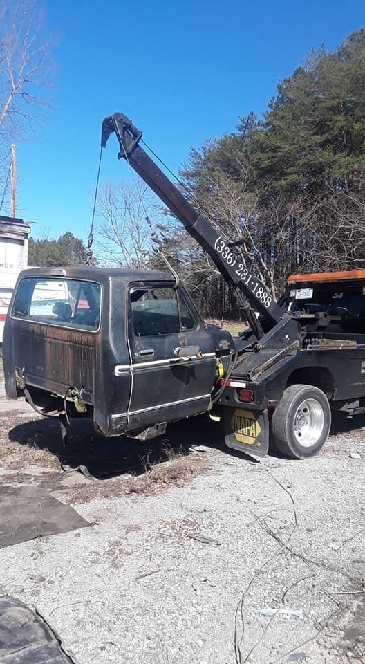 A tow truck is towing a black truck in a parking lot.