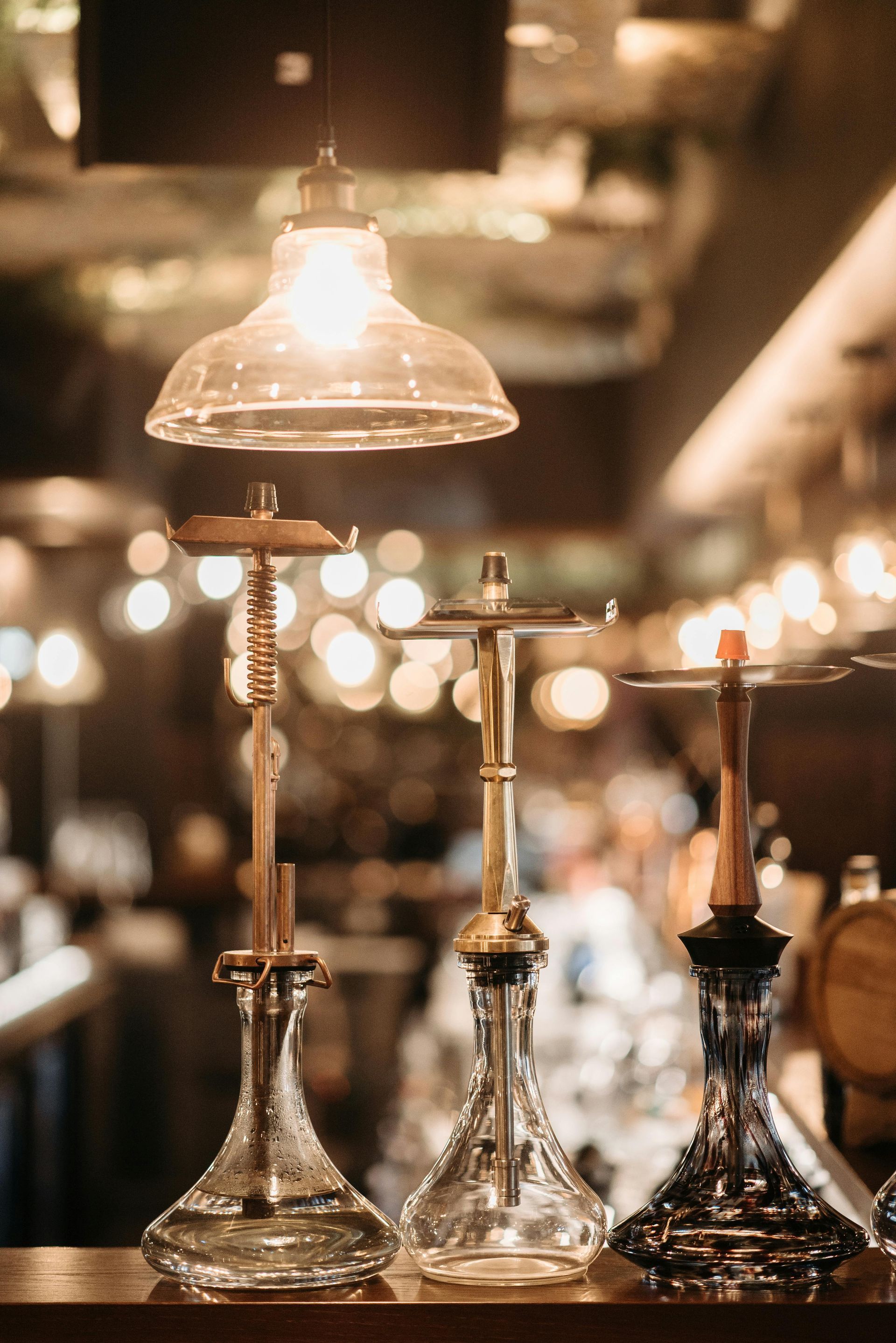 Three ornate hookahs on a bar counter, with warm bokeh lights in the background.