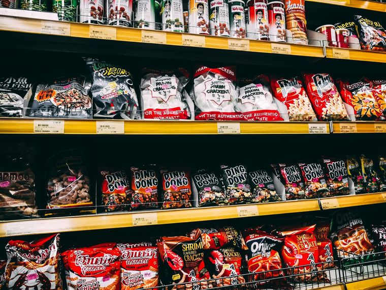 Grocery store shelf stocked with assorted packaged snacks in red, black, and white bags