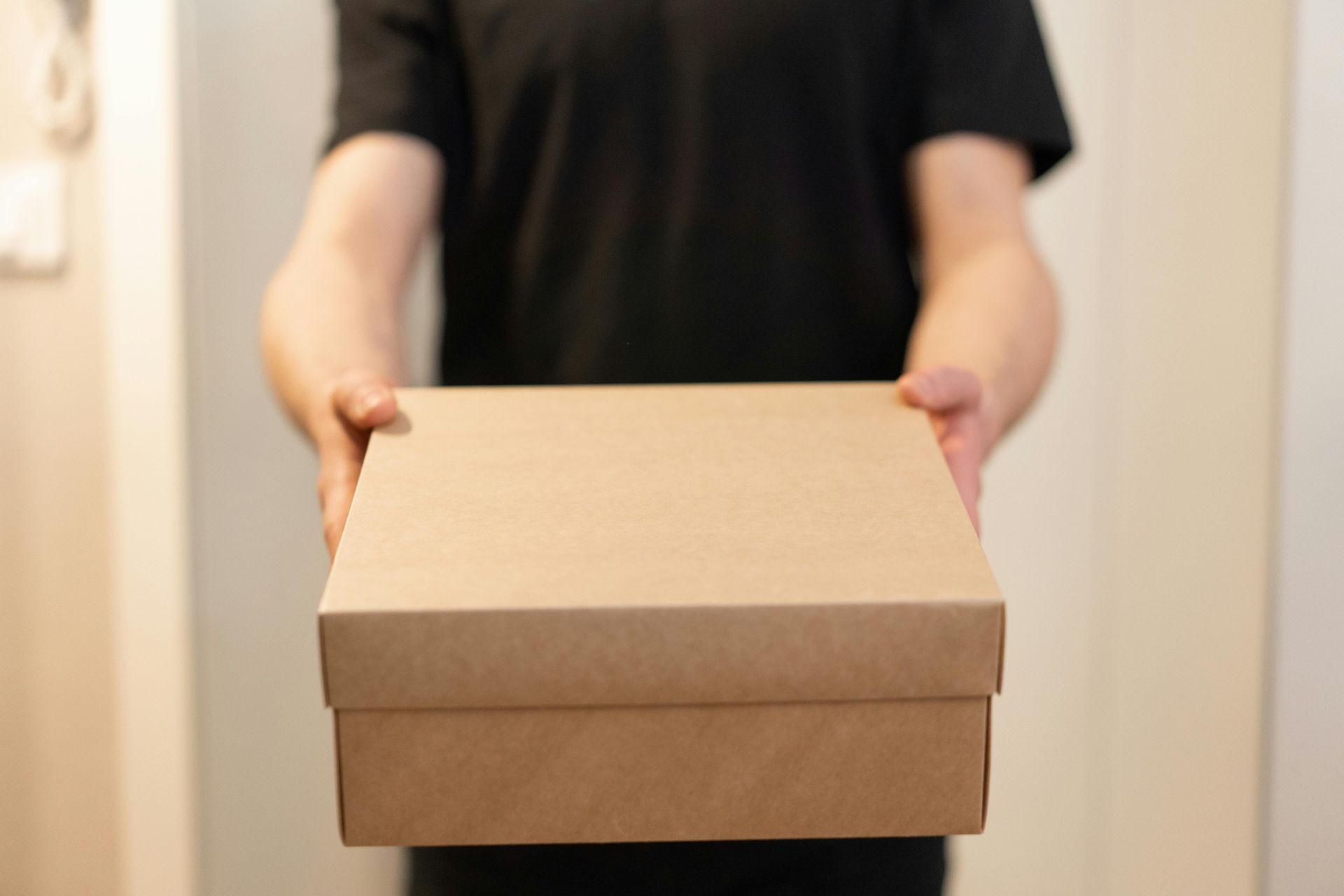 Person holding a plain cardboard box indoors.