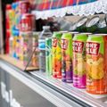 Colorful soda cans in a refrigerated store display case with a decorative lace trim.