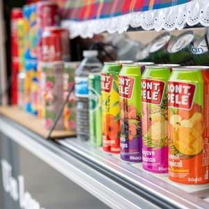 Colorful soda cans in a refrigerated store display case with a decorative lace trim.