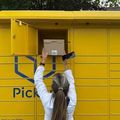 Person reaching into a yellow parcel locker to retrieve a package