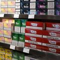 Tobacco cigarette packs stacked on store shelves, including Winston, More, and other brands with warning labels