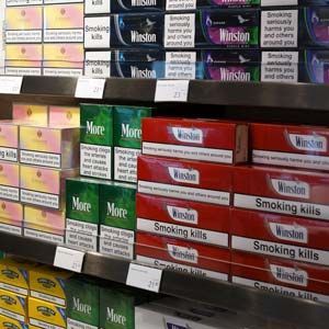 Tobacco cigarette packs stacked on store shelves, including Winston, More, and other brands with warning labels