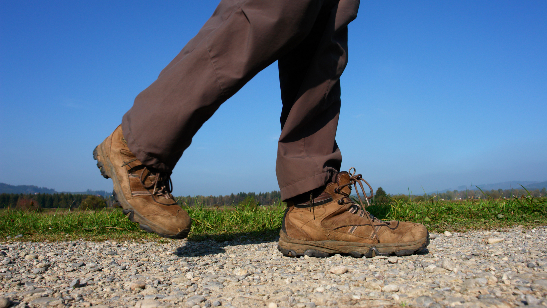 A person wearing hiking boots is walking on a gravel road.