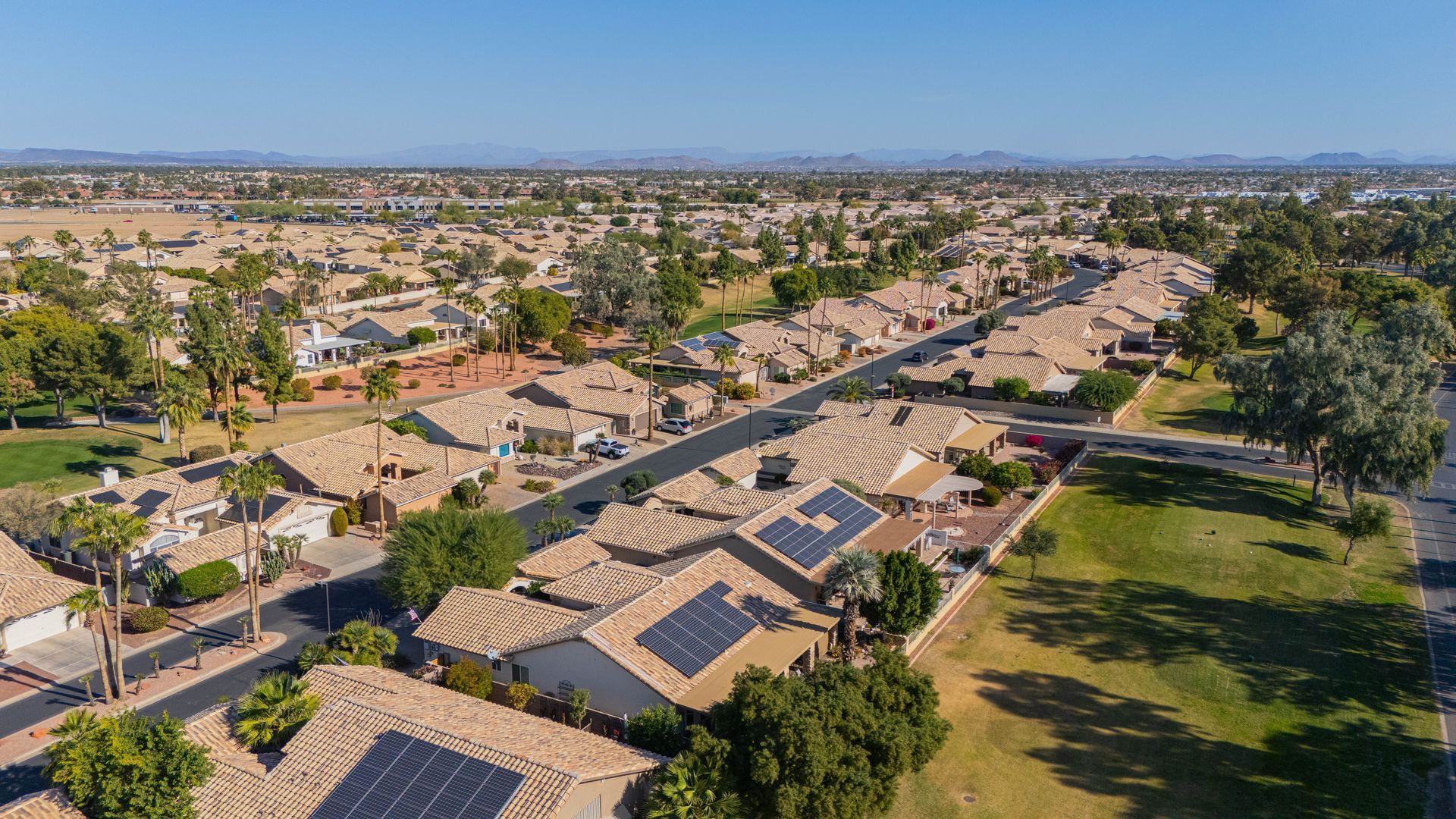 Aerial view of a suburban neighborhood with tan rooftops, trees, streets, and a green park area.