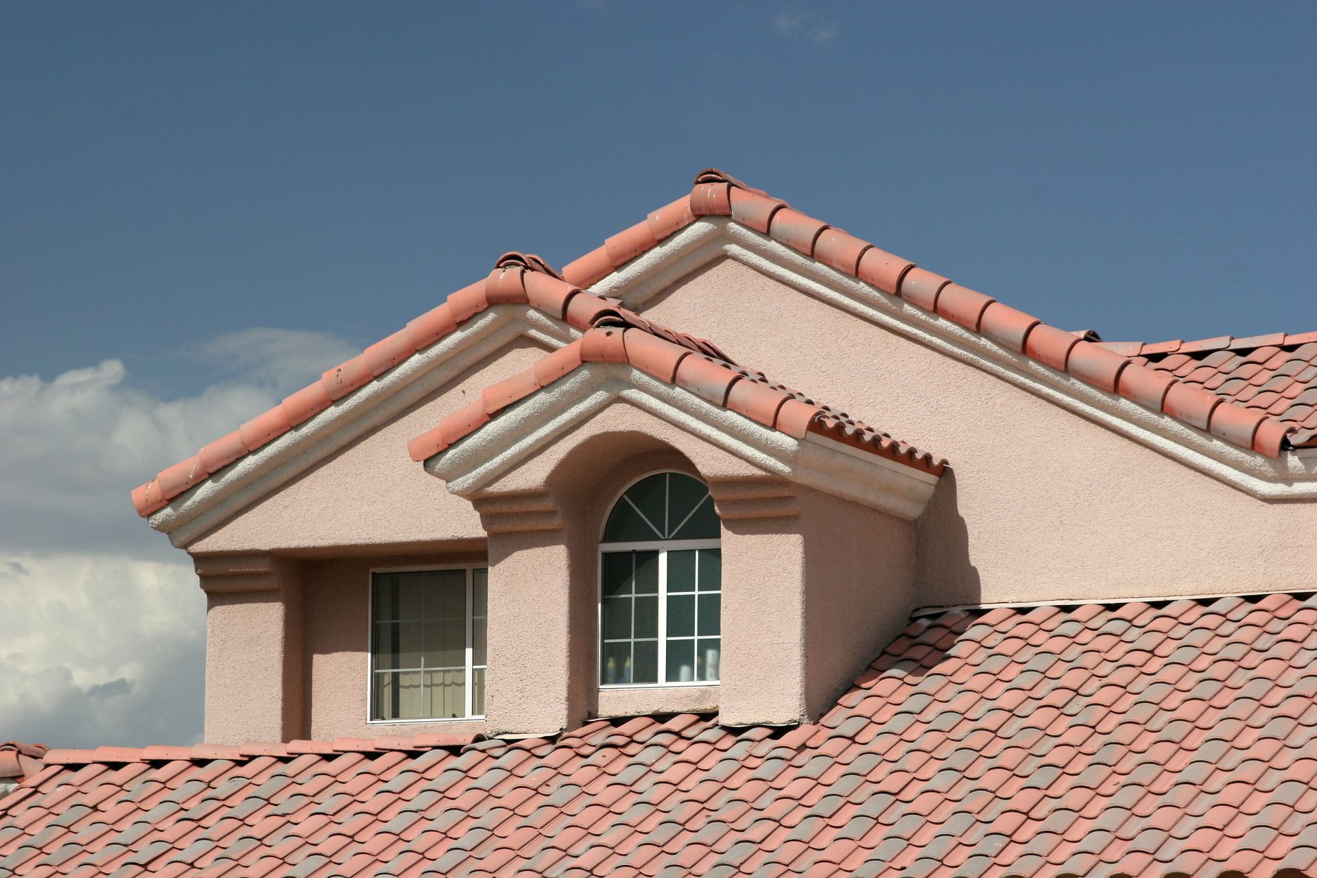 Red-tiled roof with a dormer window against a cloudy blue sky