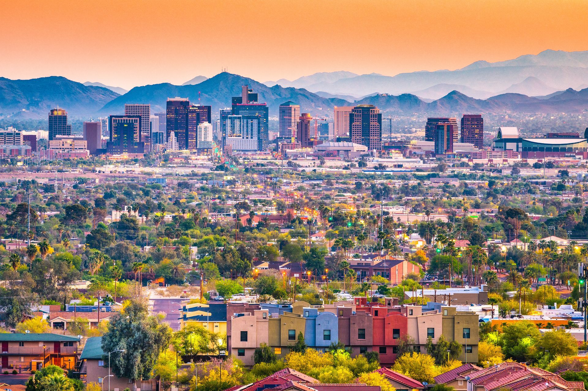 Colorful city skyline at sunset with mountains in the background and houses in the foreground