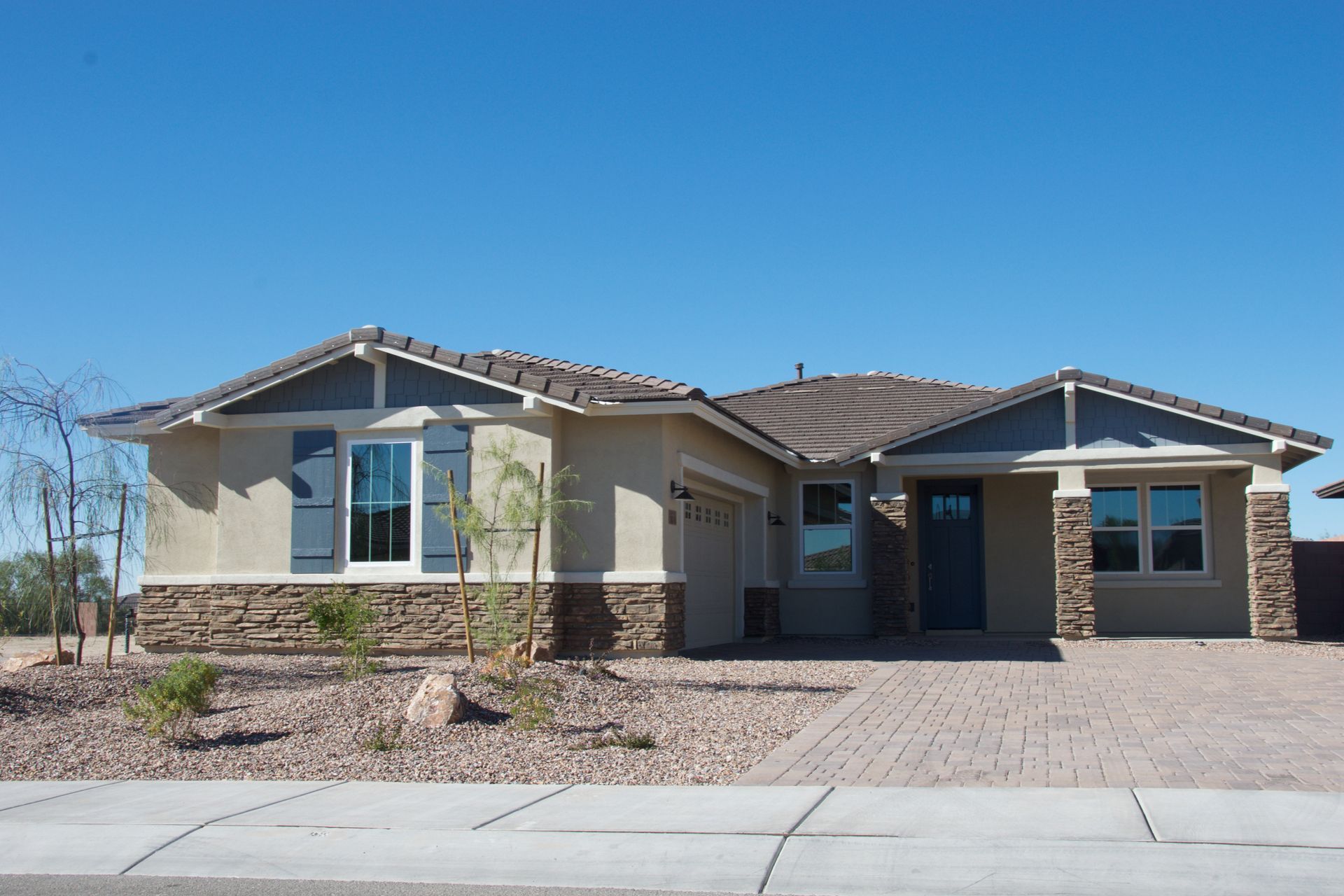 Single-story tan house with stone accents, a brick driveway, and blue sky.