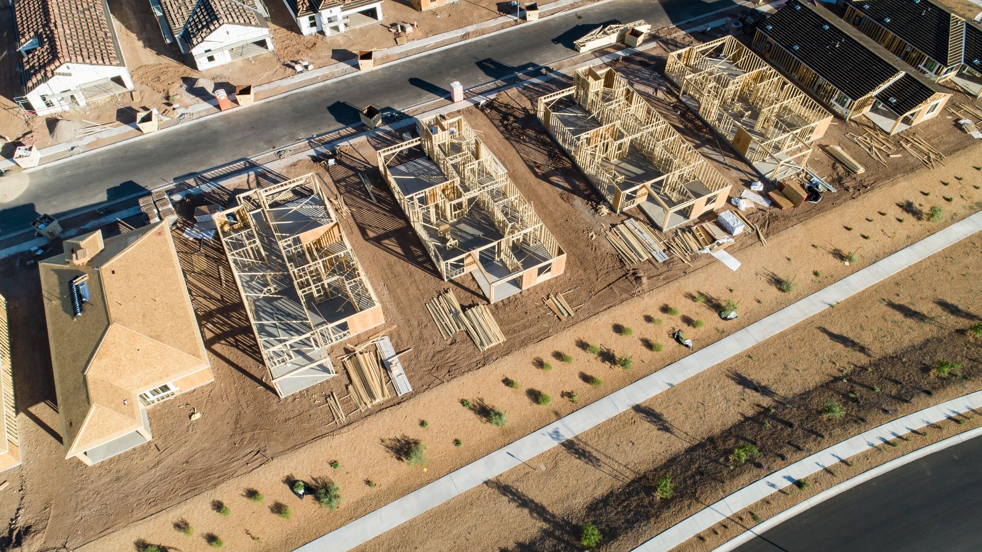 Aerial view of partially built homes in a desert neighborhood with roads and parked vehicles nearby