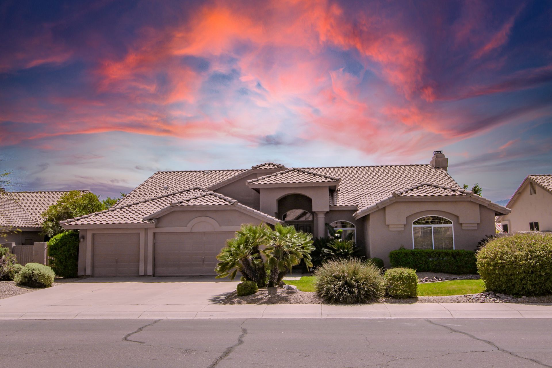 Suburban stucco house with a two-car garage under a dramatic pink and purple sunset sky