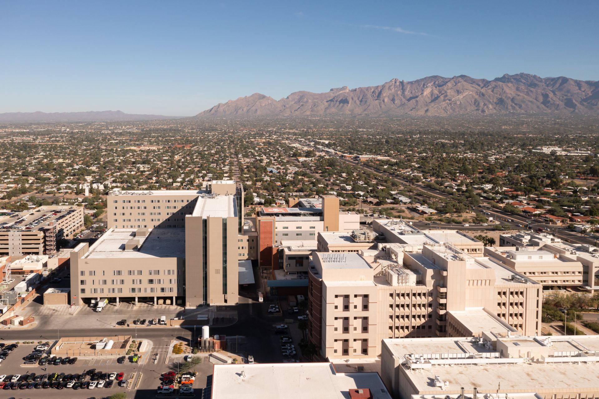 Aerial view of a large beige hospital complex in a desert city with mountains in the background