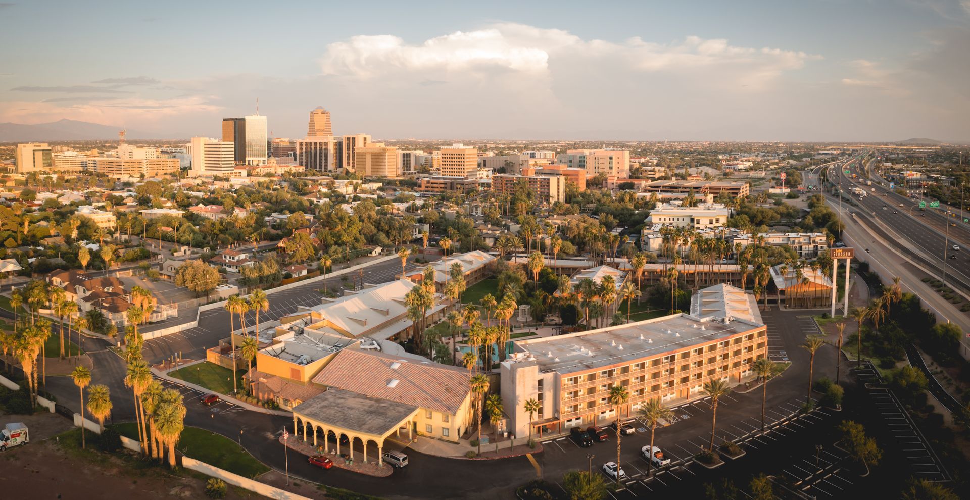 Aerial view of a sunlit city skyline with buildings, roads, and palm trees at golden hour