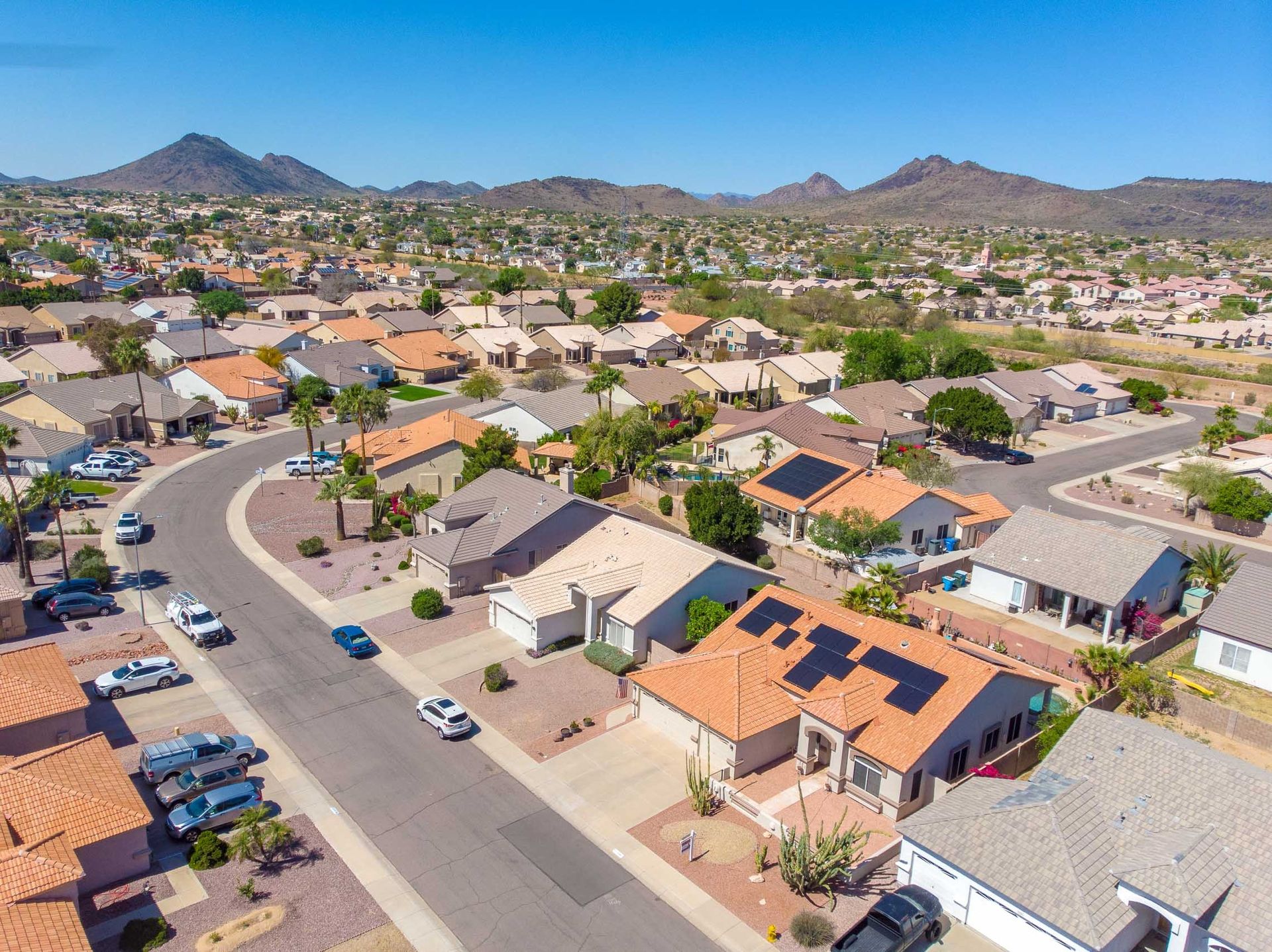Aerial view of a suburban neighborhood with houses, parked cars, and mountains in the distance.