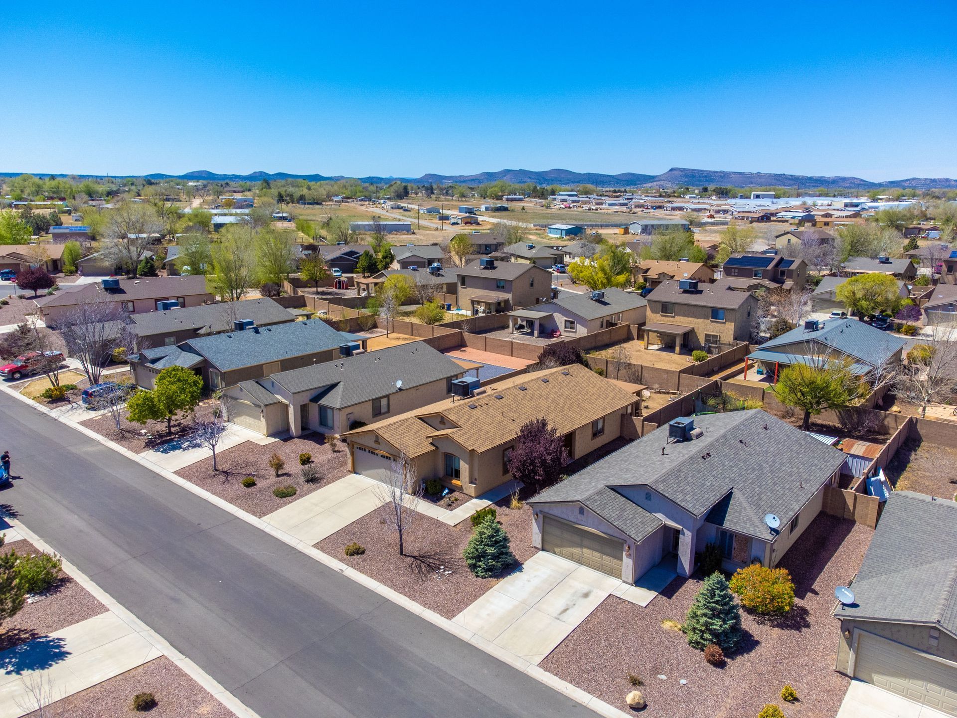 Aerial view of a suburban neighborhood with rows of houses, streets, and distant hills under a clear sky